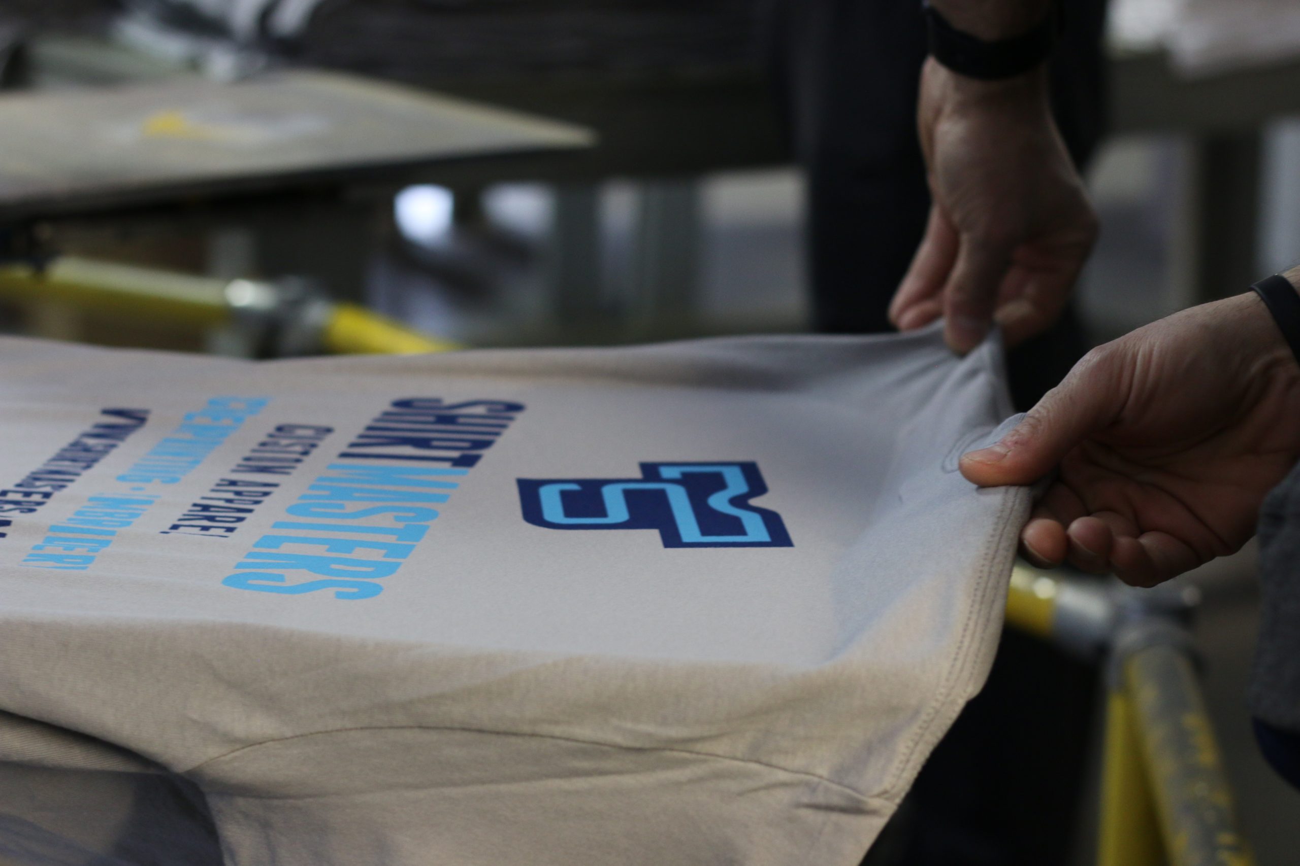A Shirtmasters tee on the printing press with a team member working at the screen